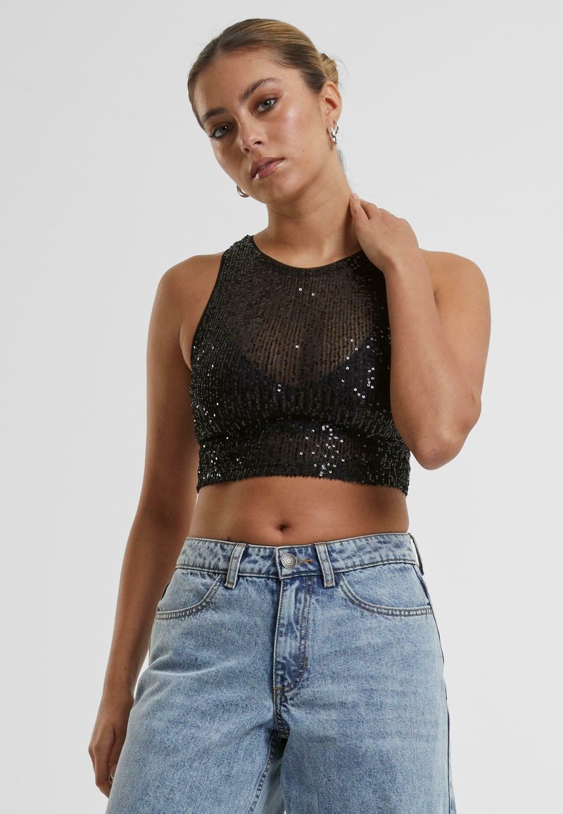 Černý flitrový crop top bez rukávů. Texturovaný, lesklý povrch s přiléhavým siluetou. V kombinaci s vysokým pasem, světle modré džíny.