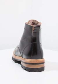 Bottine en cuir noir avec une doublure en fourrure brune douce, un bout arrondi et une semelle en caoutchouc durable avec un accent en bois stratifié.