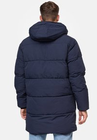 Geacă umplută bleumarin cu glugă, având un design matlasat, mâneci lungi și un tiv care se extinde sub talie. Material din poliester.