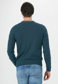 Dunkelgrüner Pullover mit rundem Ausschnitt und langen Ärmeln, mit gerippten Bündchen und Saum, kombiniert mit hellblauen Jeans.