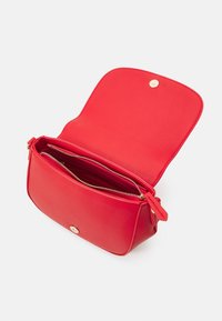 Röd läder crossbody-väska med en texturerad yta, guld detaljer, övre dragkedjestängning och ett inre fack.