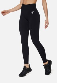 High-waisted black leggings made of smooth, stretchy material, featuring a subtle white logo on the left hip and a fitted silhouette.