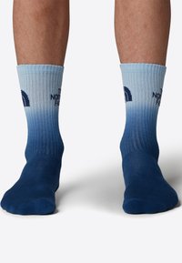 Blå gradientstrumpor med ribbad textur och ljusblå volang. Funktioner en logotyp i marinblått på ovansidan. Längd ovanför vristen.