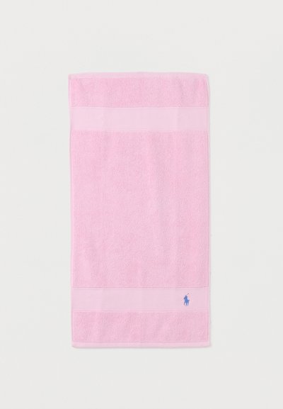Ροζ ορθογώνια πετσέτα με υφασμένες ρίγες κοντά στις άκρες και μικρό μπλε κεντημένο λογότυπο στην κάτω δεξιά γωνία.