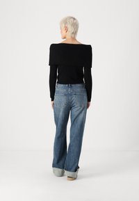 Črna off-the-shoulder rebrasta majica v kombinaciji s širokimi, zbledelimi modrimi kavbojkami z visokim pasom in razfrkanimi hlačnicami. Prikazana zadnja stran.