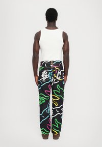 Unisex black denim pants with vibrant abstract patterns in pink, green, yellow, and blue. Features standard back pockets and a zip closure.