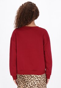 Bordó pulóver laza szabással, hosszú ujjakkal, bordázott kerek nyakkal és texturált anyagból. Leopárdmintás szoknyával párosítva.