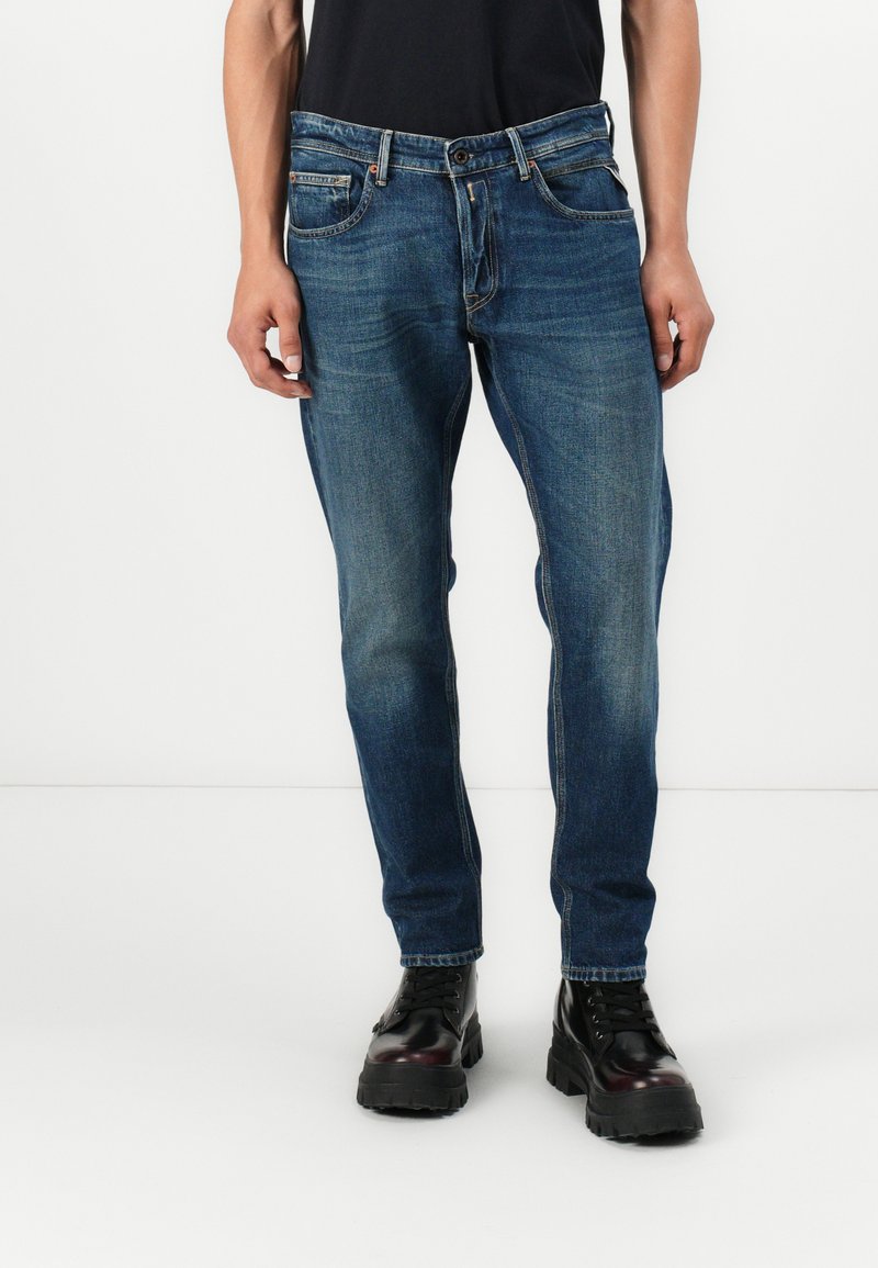 Dark blue denim jeans with a slim fit, five pockets, and slight fading. Paired with black, chunky-soled boots.