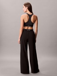 Sutiã desportivo preto com design de alças cruzadas; faixa elástica com o logótipo 'Calvin Klein'. Calças largas pretas e fluidas com um corte descontraído.