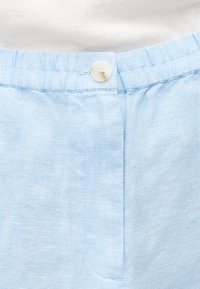 Ανοιχτό μπλε λινό παντελόνι με ελαστική μέση και ένα λευκό κουμπί μπροστά, που δείχνει την λεπτή υφή του υφάσματος.