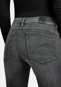 Jeans de mezclilla gris oscuro con un diseño ajustado, que cuentan con bolsillos traseros y detalles de costura sutiles. Etiqueta de cuero en la cintura con el nombre de la marca.