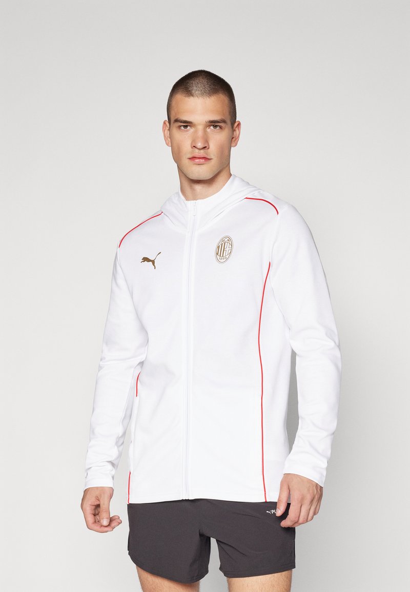 Hvid zip-up hoodie med røde detaljer og et guld logo på brystet, lavet af blødt stof, med lange ærmer og hætte.