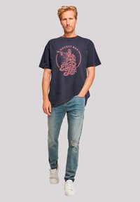 Dark navy oversized t-shirt with a pink graphic print, featuring "Rocket Man" and "Elton John." Paired with light blue distressed jeans and white sneakers.