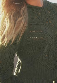 Pull en tricot vert olive avec un design texturé comprenant des motifs de feuilles et des accents en dentelle. Ourlet en côtes à la taille.