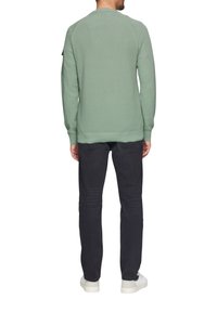 Groene sweatshirt met een gestructureerd oppervlak, raglanmouwen, ribgebreide mouwen en onderrand, gecombineerd met donkere jeans en witte sneakers.