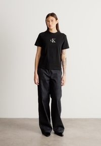 Svart bomulls-t-skjorte med logo på brystet, kombinert med høyt liv mørke denim-bukser. Antrekket har en avslappet passform og enkelt design.