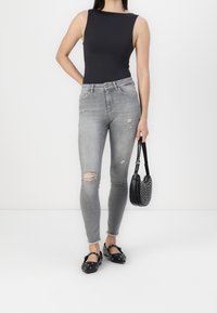 Jeans ajustados grises con rodillas desgastadas, combinados con una blusa sin mangas negra y zapatos negros. Lleva un pequeño bolso negro con tachuelas.
