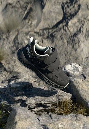 Black athletic shoe with Velcro straps, textured upper, and a gray and white sole. Lightweight design, suitable for outdoor use.