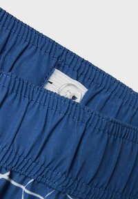 Blå shorts med elastisk midja och samlad textur, med en vit etikett med sömnad och en knappstängning för justeringar.