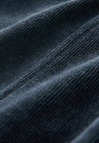 Sötétkék textúrájú szövet, látható függőleges bordázattal, puha tapintású és kissé fénylő, ami hangsúlyozza a mélységet és a dimenziót.