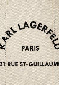 Etichetta in tela di cotone con testo in grassetto nero che recita "KARL LAGERFELD", "PARIGI" e "21 RUE ST-GUILLAUME" su uno sfondo beige.