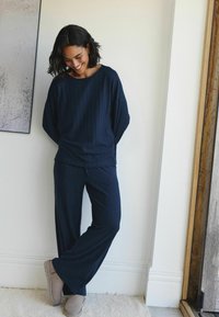 Navy-blaues Rippstrick-Loungewear-Set, bestehend aus einem lockeren Oberteil und weiten Hosen, kombiniert mit beige-farbigen Slippern.