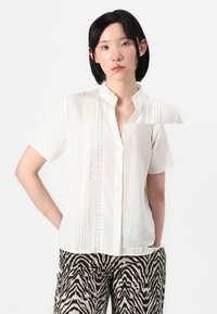 Witte blouse met korte mouwen, een gerimpelde halslijn, knoopsluiting en een gestructureerde stof, voorzien van verticale streepdetaillering en kantaccenten.
