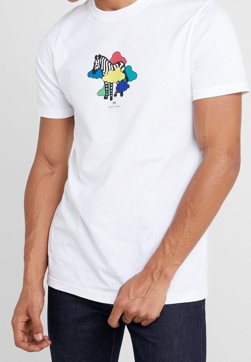 Homme portant un t-shirt blanc avec une illustration de zèbre entourée de formes de nuages colorées en bleu, rouge, jaune, vert et sarcelle.