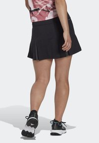 Falda de tenis negra con pliegues, combinada con una camiseta colorida. Tiene una cintura ceñida y se lleva con zapatillas deportivas negras y azules.