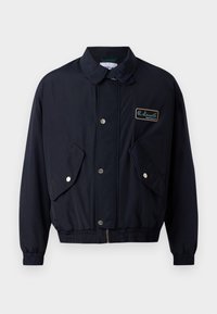 Marineblaue Jacke mit einem Frontreißverschluss, Druckknöpfen, zwei seitlichen Taschen und gerippten Bündchen. Ausgestattet mit einem Logo-Patch auf der linken Brustseite.
