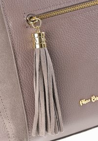 Tassel sleutelhanger met een gouden kap bevestigd aan een gouden ritssluiting op een handtas van getextureerd taupekleurig leer en suède.