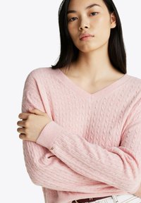 Maglione a maglia cable, con scollatura a v, di un rosa tenue. Realizzato in un tessuto testurizzato con polsini a coste. Presenta un piccolo dettaglio sul polsino.
