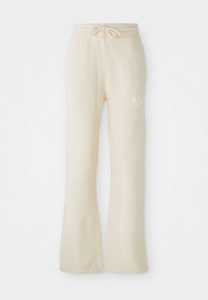 Pantalons de sport couleur crème avec une texture douce, dotés d'une taille à cordon de serrage et de jambes évasées. Détail de logo subtil sur la hanche gauche.