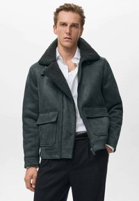 Giacca in shearling grigio scuro con ampio colletto, chiusura con zip e due tasche frontali. Texture morbida e design strutturato.