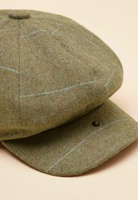 Zelená čiapka z tkanej látky v rybej kosti s guľatým vrchom a malým šiltom, zdobená modrými a ružovými akcentmi a detailom z kovového gombíka.