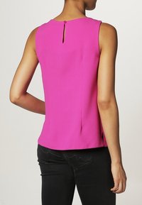 Fuchsia ärmlös topp med rund halsringning och detalj med nyckelhål bak. Slät textur och skräddarsydd passform, i kombination med svarta byxor.