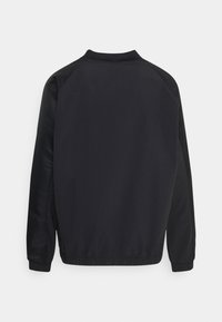 Svart jacka med raglanärmar, elastiska mudd och nederkant. Slät tyg med matt finish, med en subtil logotyp på ärmen.