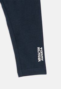 Tamsiai mėlynos legging'ų kelnės, pagamintos iš švelnios medvilnės, su prigludusia forma. Apatinėje koja pusėje yra baltas tekstas, o audinys yra lygus ir elastingas.