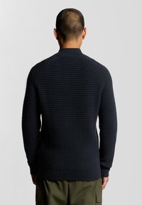Maglione lavorato a maglia blu scuro con un motivo strutturato a coste, scollo rotondo e maniche lunghe, progettato con una vita e dei polsini aderenti.