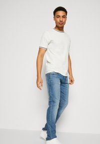 White short-sleeve t-shirt with a navy striped collar, paired with blue jeans and white sneakers, featuring a slim-fit design.