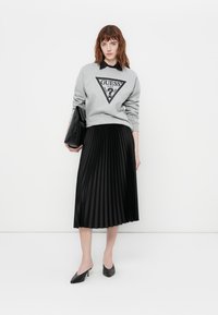 Pelēka sporta jakas ar trīsstūra grafiku un melna plīša svārki. Melna norādītā toe zābaki un melna clutch soma papildina tērpu.