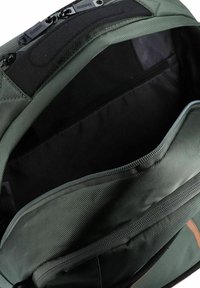 Interior de mochila verde oliva que muestra un compartimento espacioso con un forro negro, un bolsillo con cremallera y material texturizado.