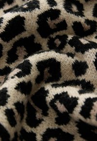 Tessuto a maglia con motivo leopardato, caratterizzato da grandi macchie nere su uno sfondo beige, con un aspetto morbido e testurizzato.