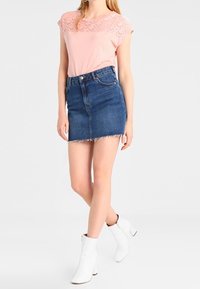 Haut rose à manches courtes avec détail en dentelle texturée, associé à une jupe mini en denim bleu foncé et des bottines blanches à talons épais.