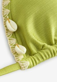 Primo piano di un tessuto verde chiaro brillante con frange beige e due decorazioni in conchiglia bianca.
