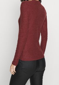 Bordowy prążkowany sweter z długim rękawem, dopasowany krój, okrągły dekolt, miękka tekstura, z bocznymi rozcięciami, zestawiony z czarnymi dopasowanymi dżinsami.