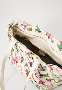 Borsa a tracolla con motivo floreale, dotata di un'esterno in cremoso tessuto intrecciato, manici robusti e una tasca interna con zip.