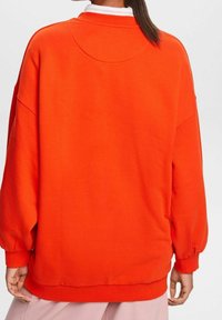 Sudadera roja de gran tamaño con una textura suave, puños acanalados y un cuello redondo, con un diseño sencillo sin logotipos visibles.