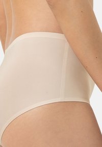Beige high-waisted onderbroeken van glad, rekbaar materiaal. Heeft een naadloos ontwerp met een schone, afgewerkte tailleband en beenopeningen.