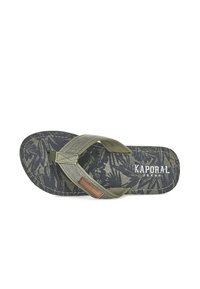 Khaki flip-flop with patterned sole featuring dark leaf motifs. Fabric straps with textured accents and logo detail. Flat, rounded footbed.